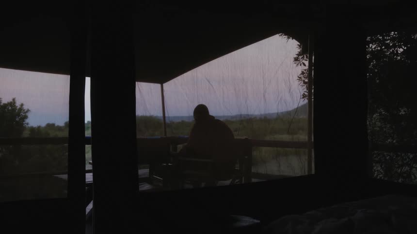 Person sits at table outside screened panels on balcony overlooking water