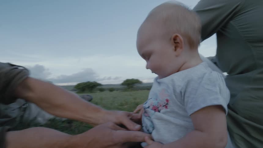 Dad tickles his baby daughter making her laugh while they are all relaxing in the grass