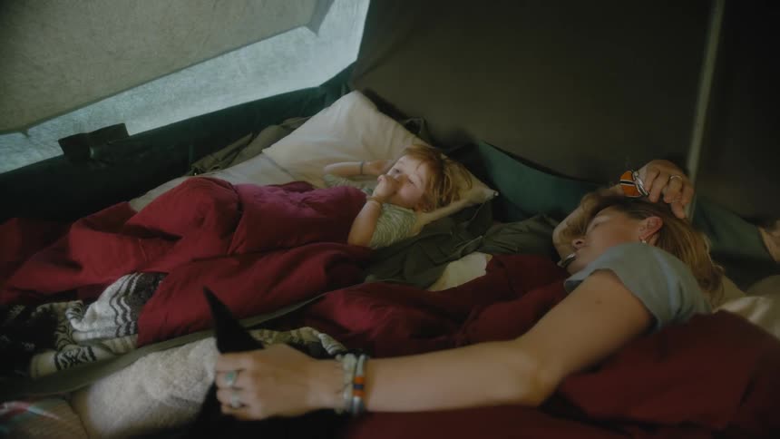 Mom reaches over and touches her sons head as he sucks his thumb