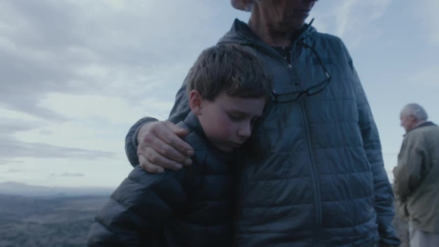 Grandfather hugs and consoles granson while standing onver a hill near the badlands at evening
