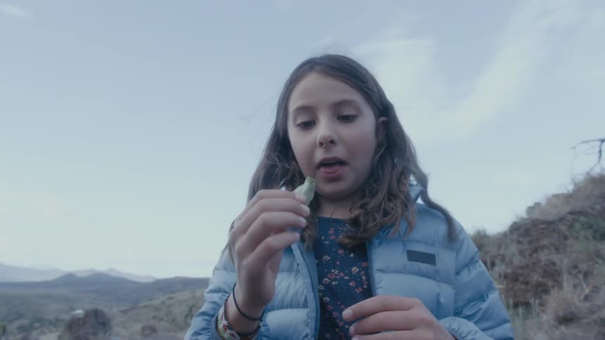 A woman shows her grandchildren how to eat a leaf as they stand in the wildnerness