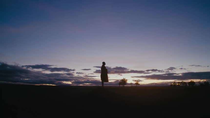 Man standing alone at the middle of an empty field outdoors during sunset