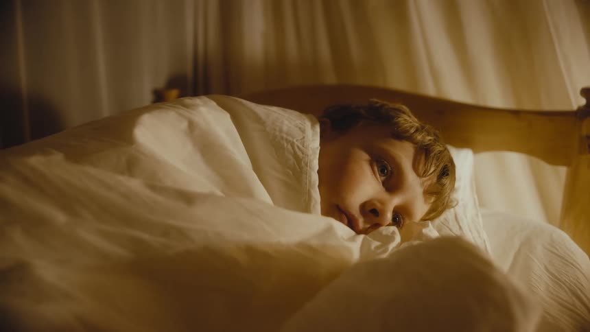 Boy lying in the bed cover with a blanket with his eyes open