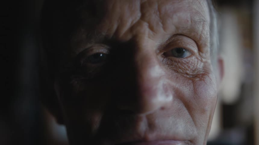 An older man with deep wrinkles in his brow looking straight ahead