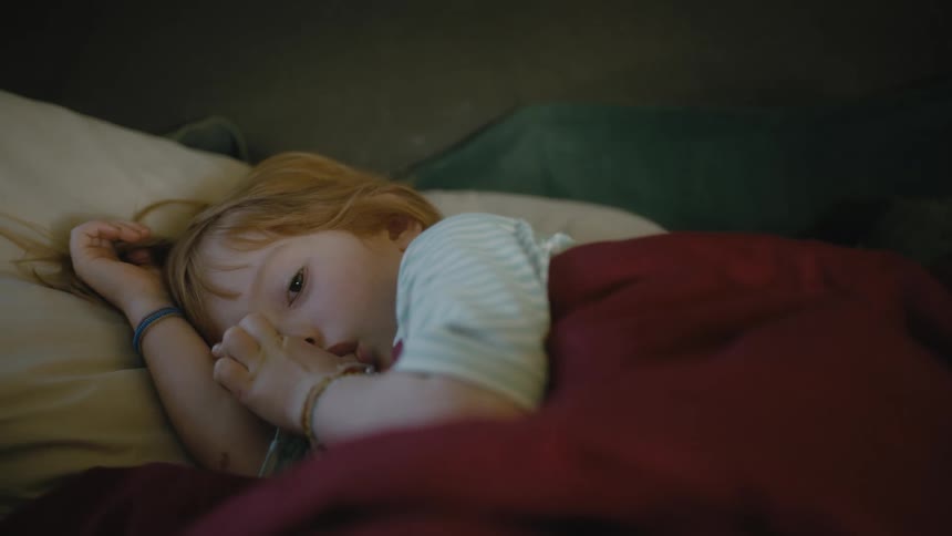 Little girl lying on her side covered by a blanket sucking her thumb