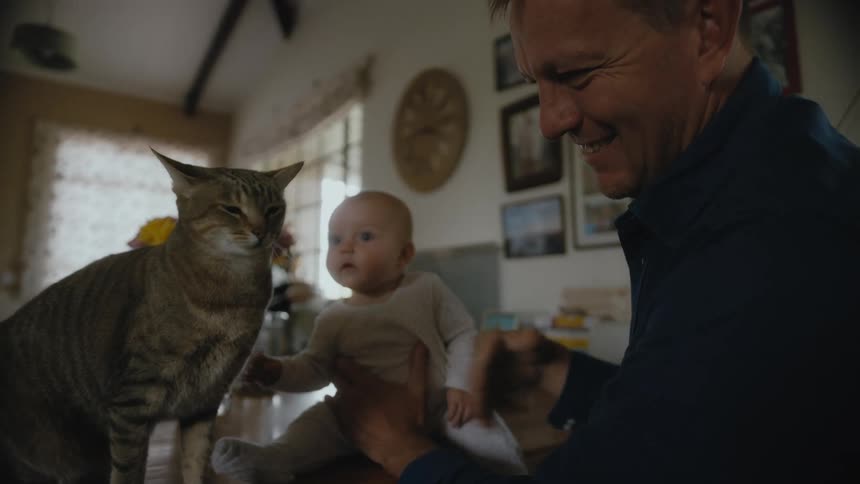Man sitting with a baby on a table at home playing with a cat