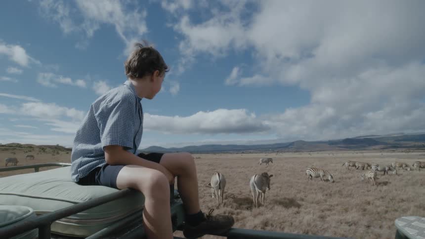 A boy is sitting on a moving truck during the daytime