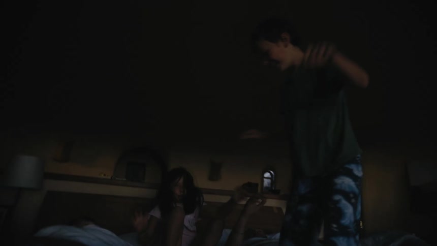 Parents lying in bed watch as their kids jump up and down on bed for a while