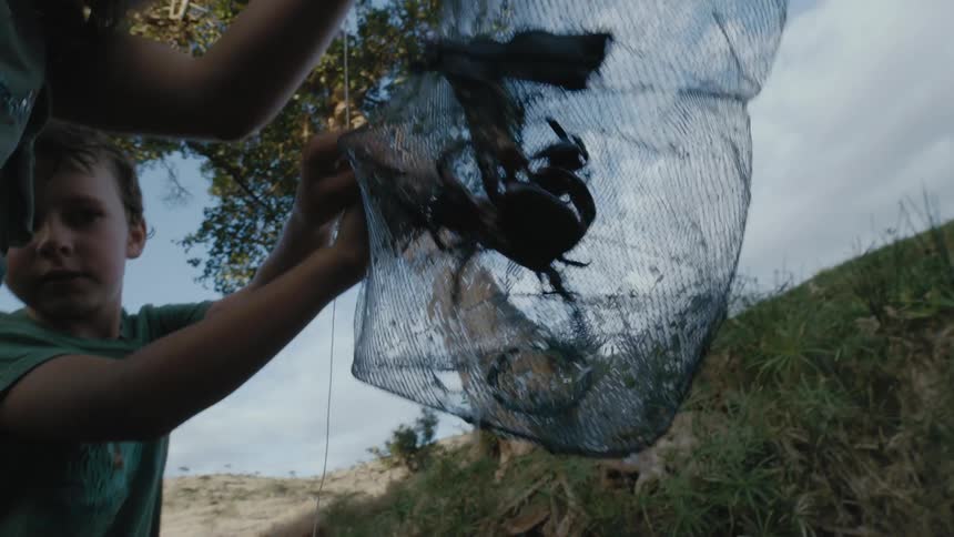 Two children look at a crab in a trap