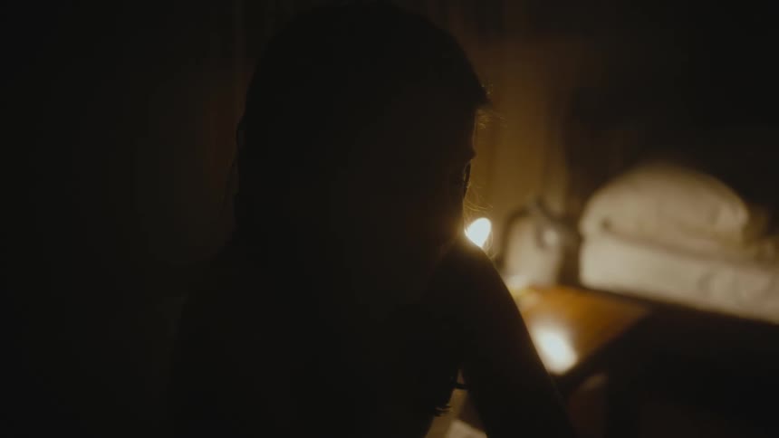 Little girl sitting on her bed in a dark bedroom with her face covered by the shadow