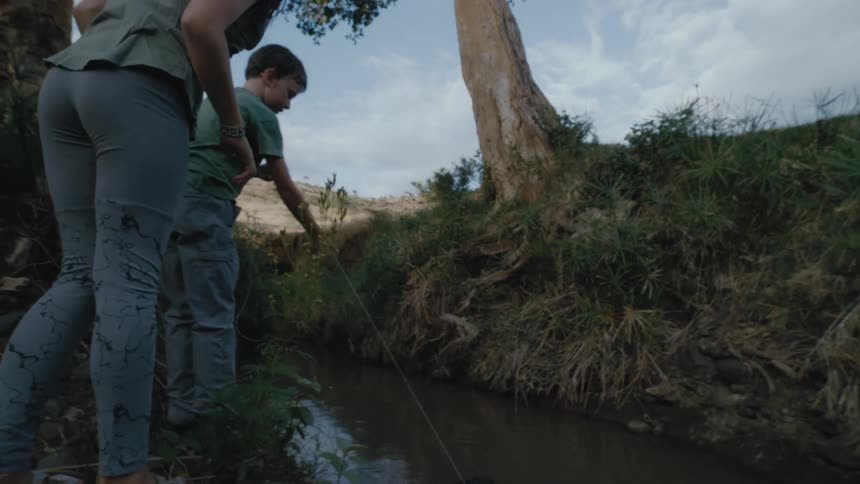 Man and woman are fishing by a creek outdoors