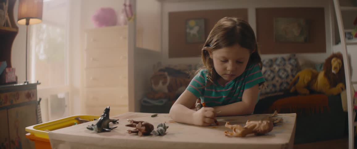 Little girl colors with crayons while sitting at a table in a playroom