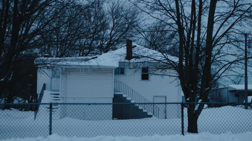A house with a snow covered yard and bare trees with a chain link fence around it