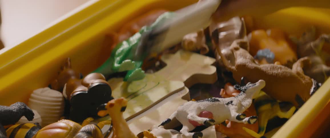 A child picks up a toy rocket from a toybox full of plastic animals