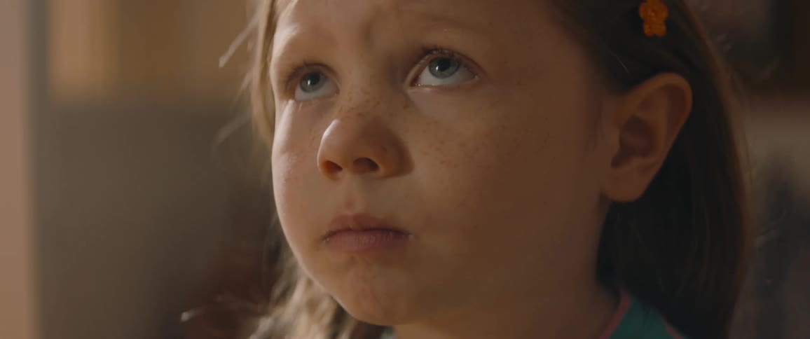 A little girl sits indoors with a worried look on her face during the day