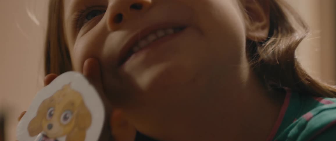Little girl with freckles and brown hair holds toy and smiles in room