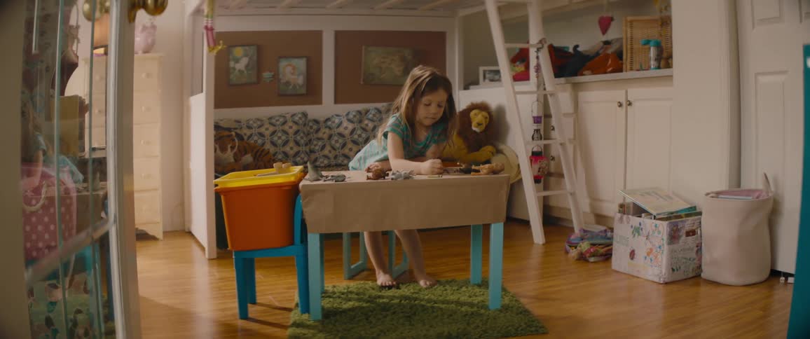 A little girl is standing over her desk coloring with crayons