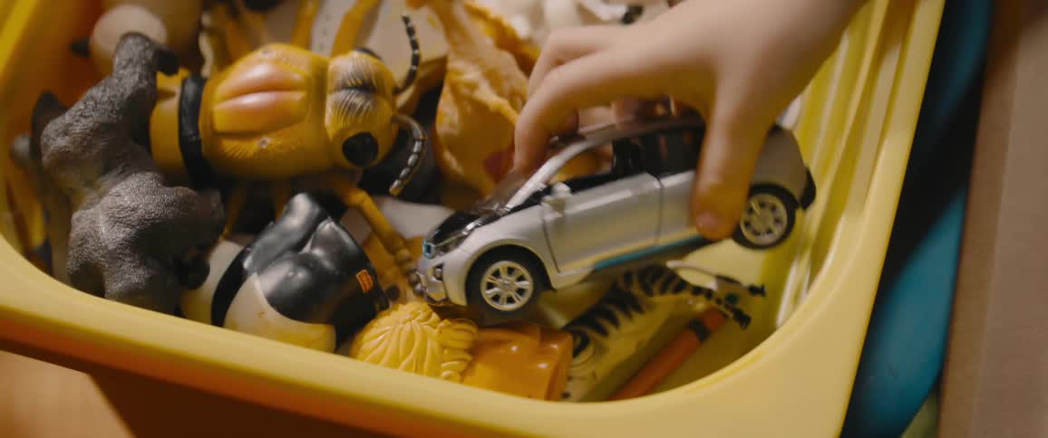 There is a yellow bin filled with toys and a child takes a toy car
