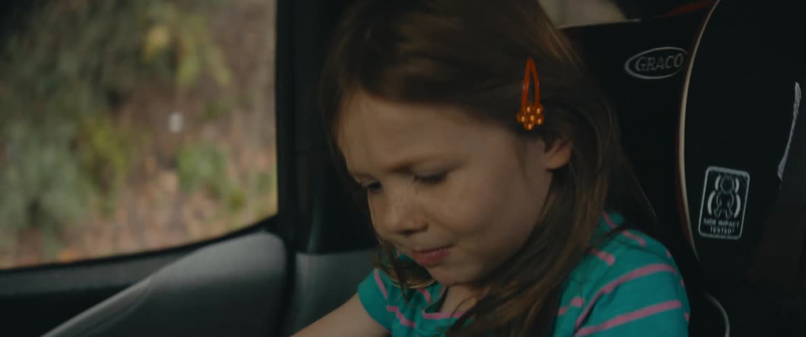 Little girl sits in a car seat in a car and plays with a toy car and angrily wipes at the bottom of the toy car