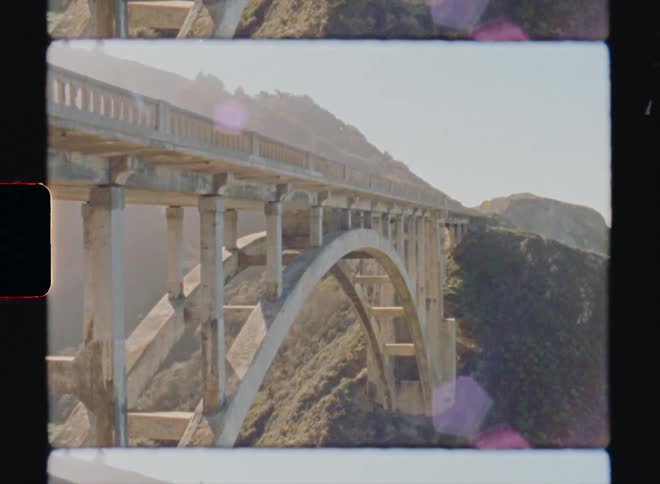 Arch bridge connects onto mountain slope on bright sunny day Big Sur California Super8 4k Film Scan