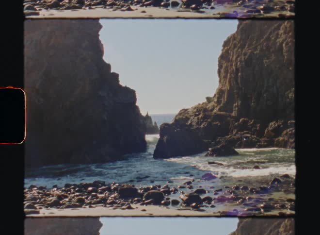 The tide washes around a rock formation into a beach covered in stones Big Sur California Super 8 4k Film Scan