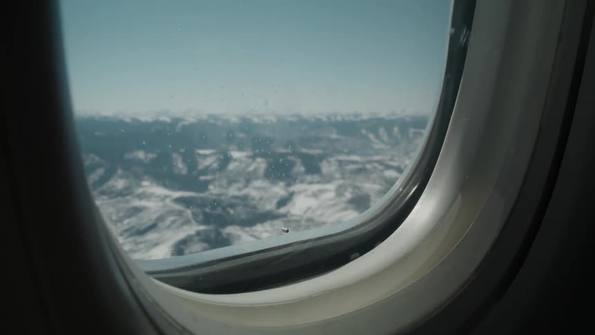 Airplane window shows snow covered mountainous terrain
