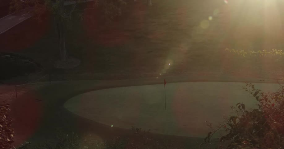 The sun shines brightly on a golf course as a flag waves near a hole
