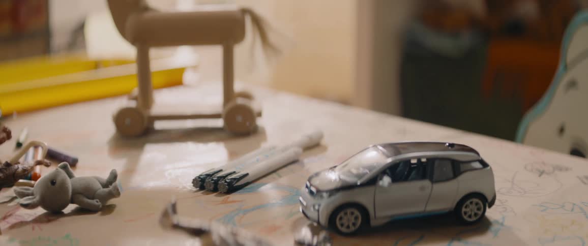 A wooden toy horse stands next to a car and dinosaur on table in room