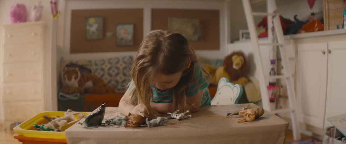 Little girl sits at a table in a playroom and colors with a crayon
