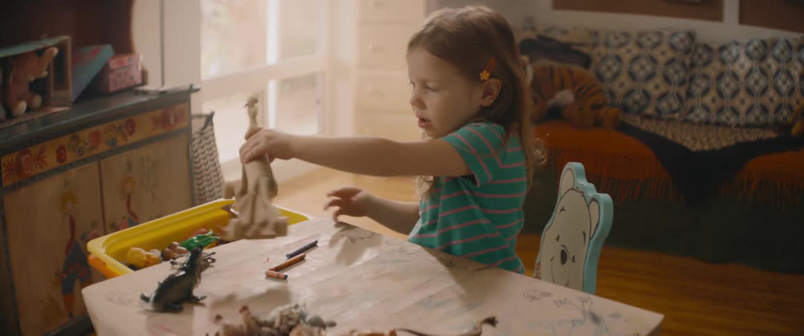 A little girl is sitting at her desk playing with a wooden toy horse