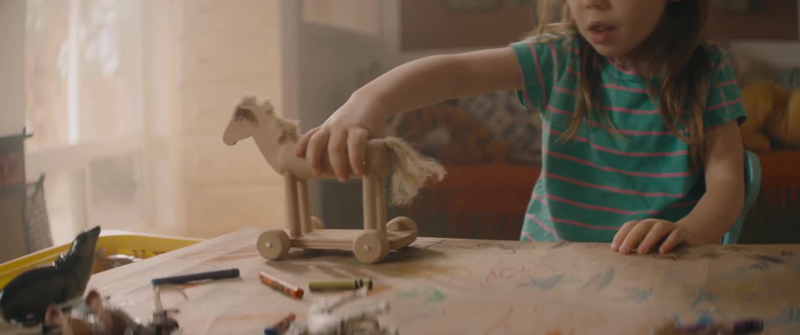 Little girl plays with a wooden toy horse on a table in the playroom