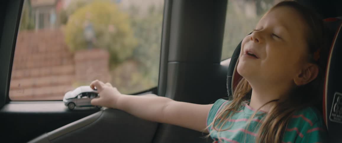 A little girls holds a toy car in her hand as she smiles and laughs during a car ride