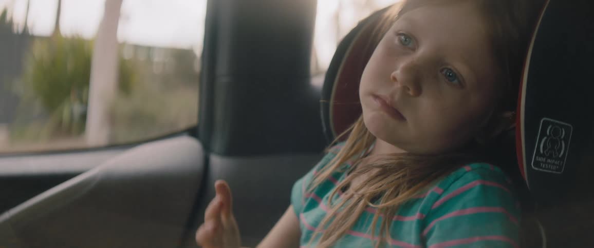A bored young girl complains while sitting in a car seat in a vehicle during the day