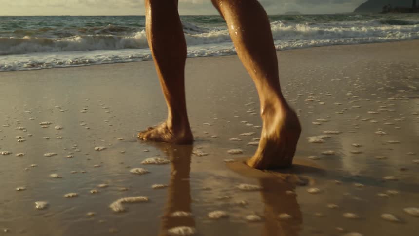 A person is walking barefoot on the beach at dusk
