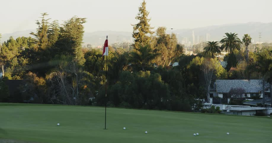 Golf balls rest beneath a flag pole on a golf course