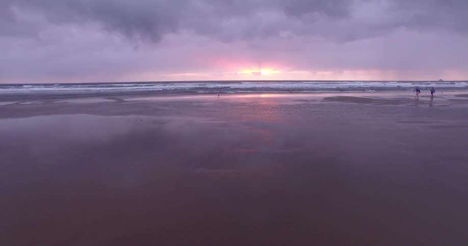 People walking on a wet beach at sunset
