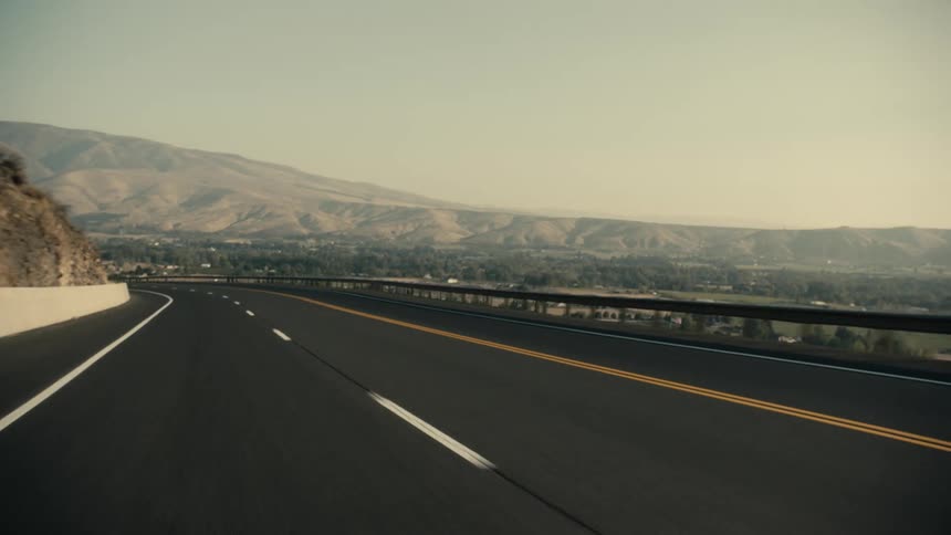 Empty highway with fields and mountains in the distance