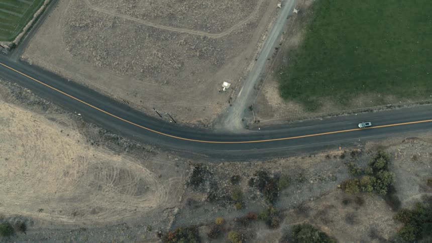 Aerial view of a white automobile traveling on a rural road