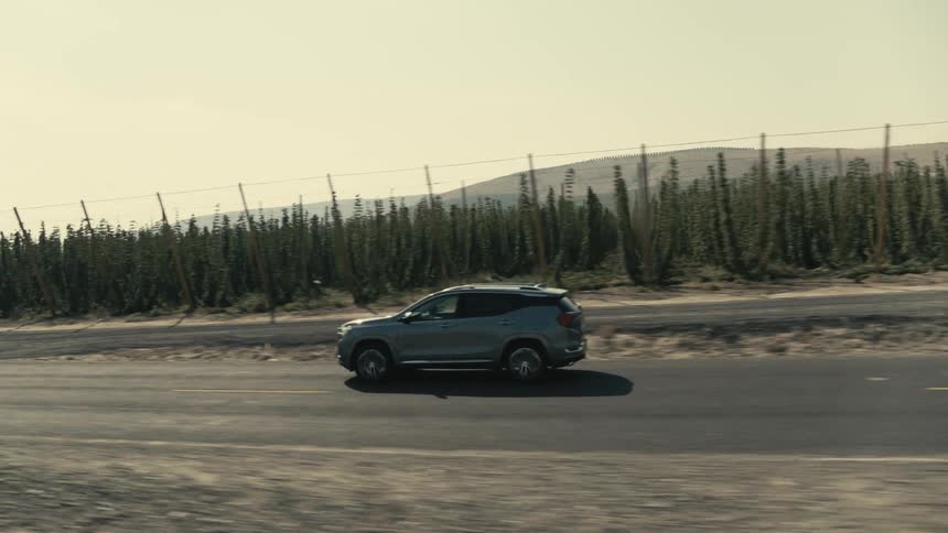 An suv travels on an empty road past fenced off crops
