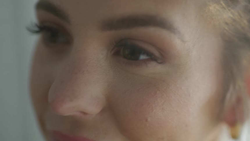 Woman with an earring in her left ear raises her eyelids and smiles