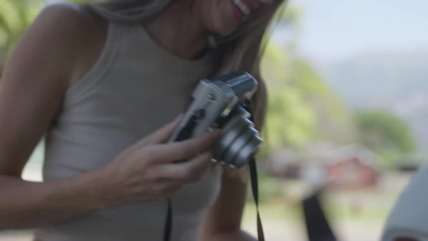 A woman with a camera holds an instant photo and shakes it before setting it down