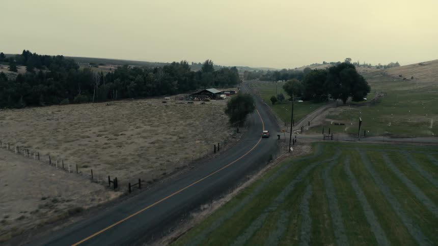 Aerial view of an automobile traveling on a rural road past buildings and trees