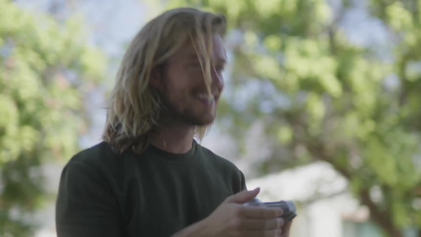 A man smiles and talks as he takes an instant photograph outside