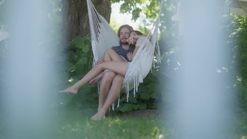 A couple sitting and cuddling on a backyard hammock