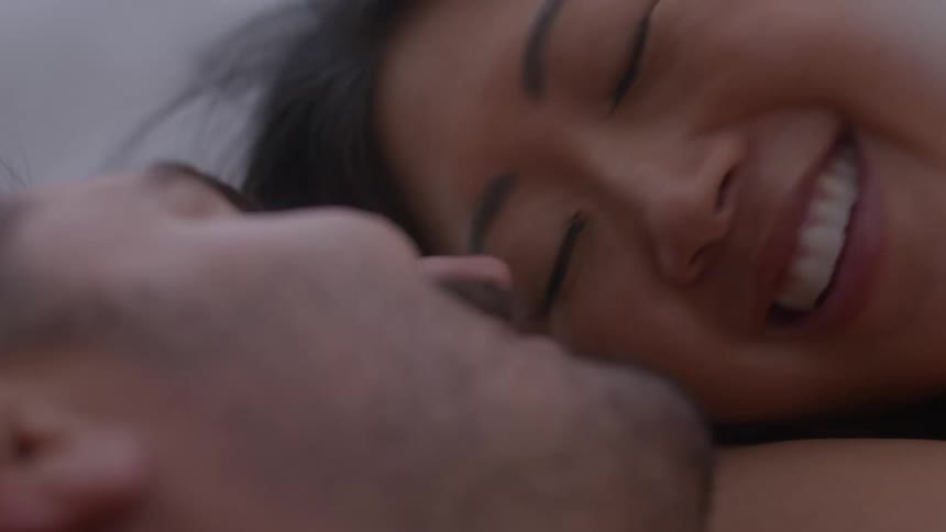 Smiling couple lie down together kissing and cuddling