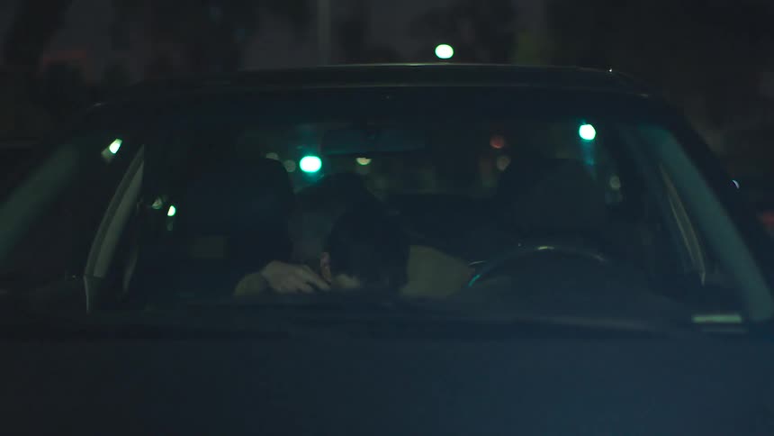 A man in the drivers seat hugs his female passenger at night