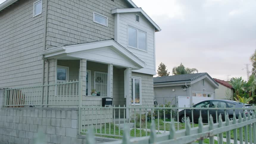 Picket fence leads to a two story house with a dark colored car parked in the driveway