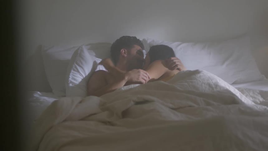 Couple lies in bed kissing and cuddling
