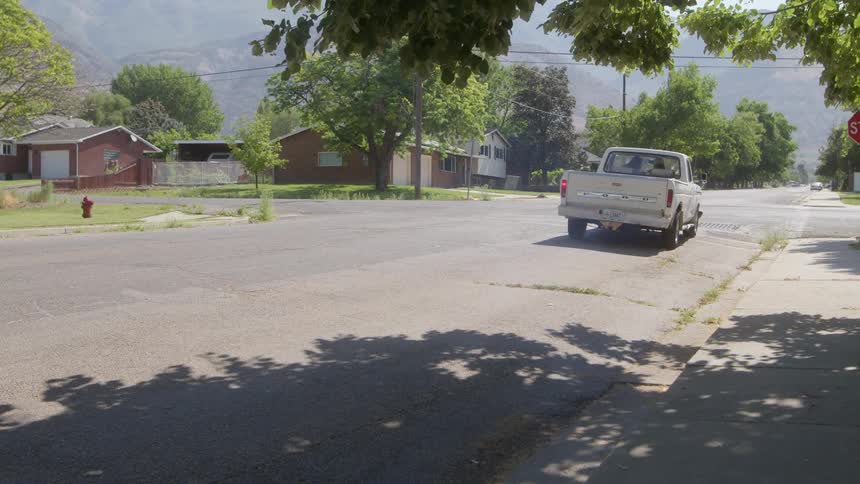 A white pickup truck is sitting on the side a neighborhood street and it drives away