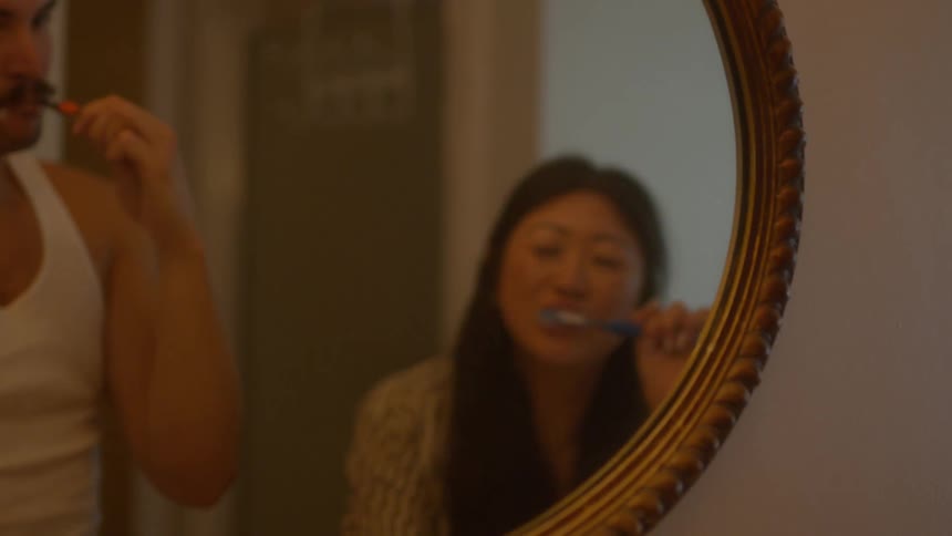 A man and woman brush their teeth in the mirror